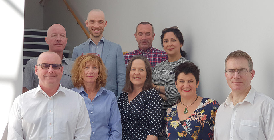 A team photograph of the current staff at the Christchurch office of Pedersen Read. They are standing in a well-lit stairwell with very light grey or white walls.